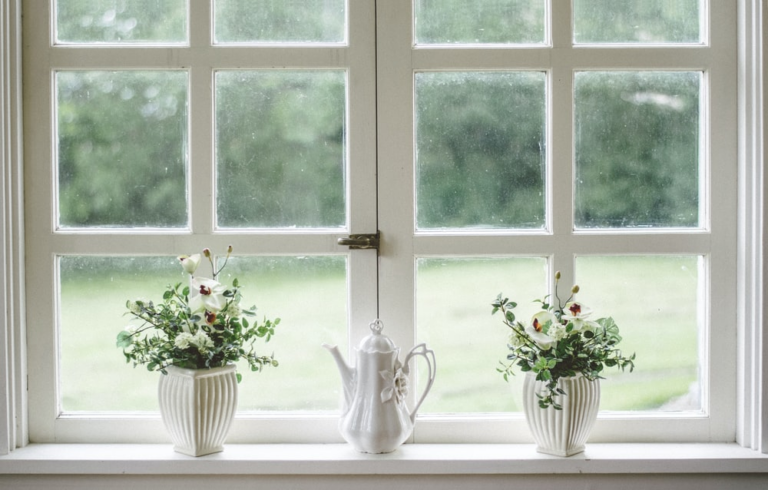A White-painted Window Featuring Two Potted Plants, One Decorative Teapot, and Rectangular Panes Requiring Professional Window Cleaning