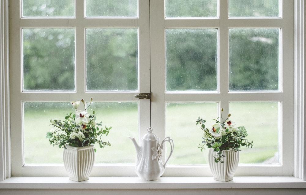 A White-painted Window Featuring Two Potted Plants, One Decorative Teapot, and Rectangular Panes Requiring Professional Window Cleaning